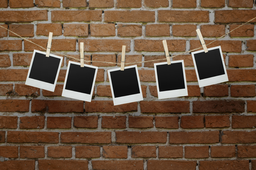 Five blank photographs hanging on a clothesline over bricl wall