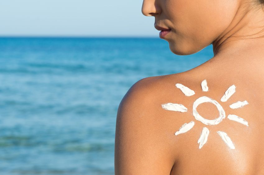 woman with sunblock in the shape of the sun on bare shoulder against ocean backdrop