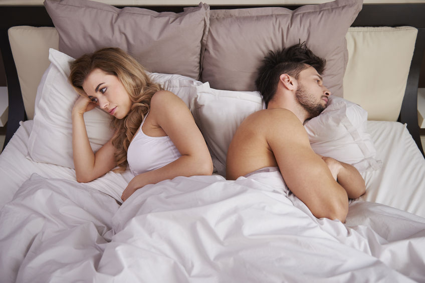 woman and man in bed facing away from each other, frustrated