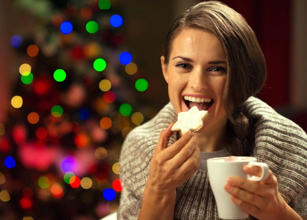 Happy woman eating Christmas cookie and drinking hot chocolate