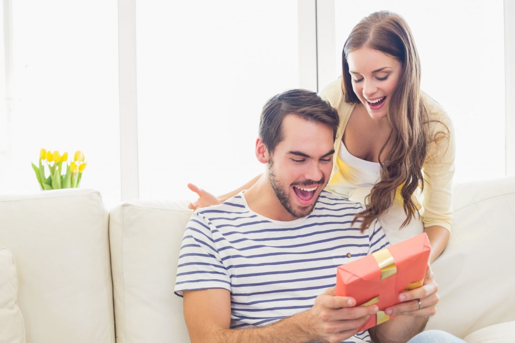 woman surprising her boyfriend with gift at home in the living room