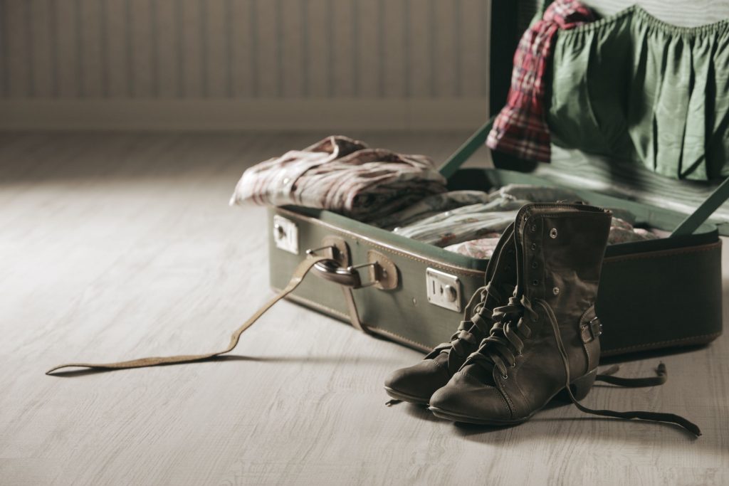 open suitcase with clothes and boots on wooden floor